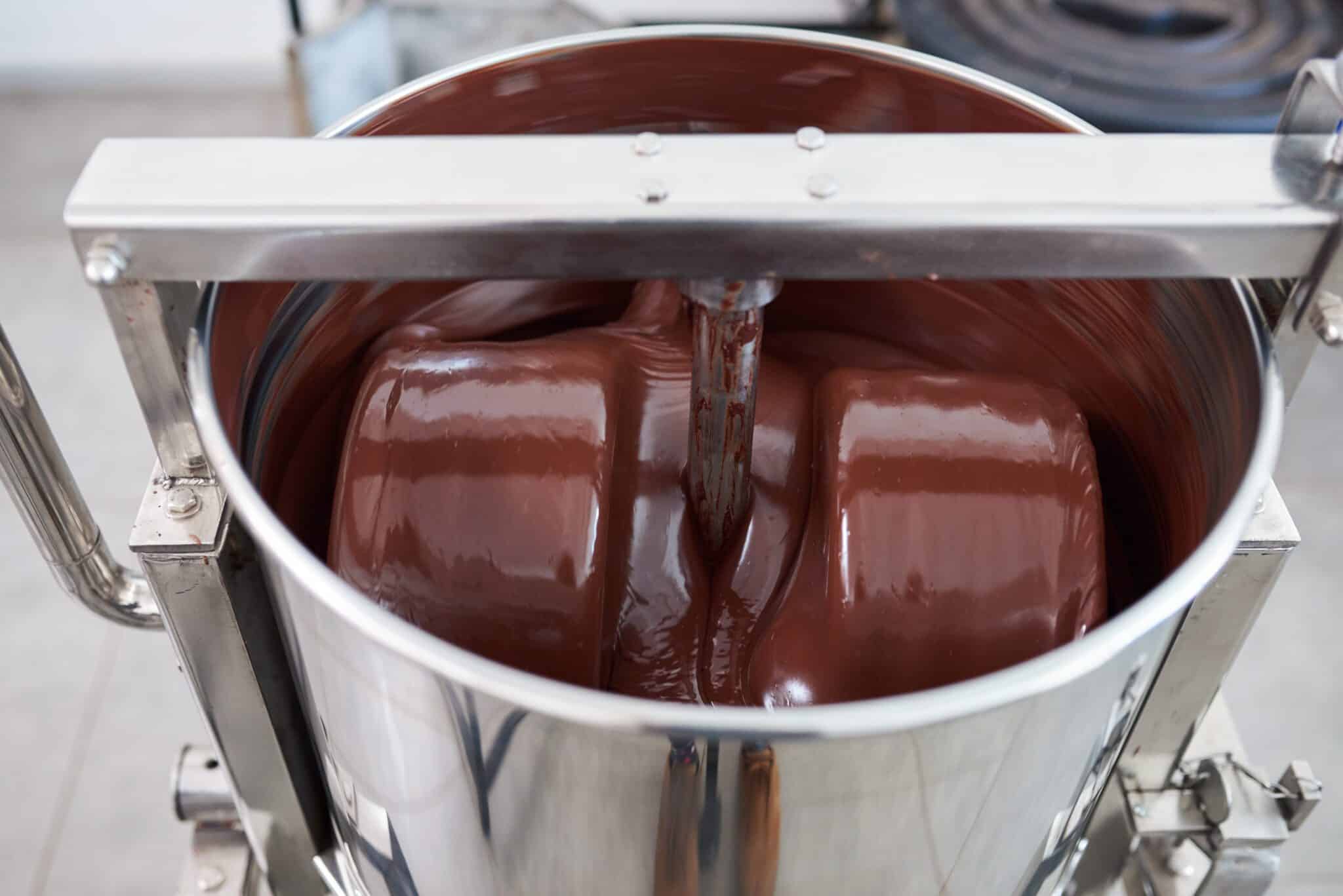 Closeup of large stainless steel mixer in an artisanal chocolate production factory turning melted chocolate